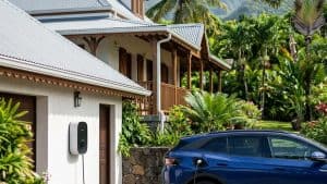 Voiture électrique bleue en recharge devant maison tropicale